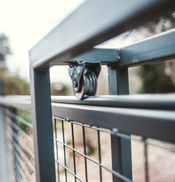 metal gate's sliding mechanism, featuring a small steel wheel set in a bracket attached to the upper frame, rolling along a rail to allow the gate to glide open.