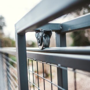 metal gate's sliding mechanism, featuring a small steel wheel set in a bracket attached to the upper frame, rolling along a rail to allow the gate to glide open.