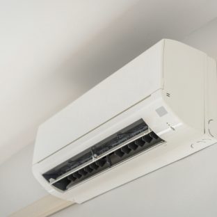 A modern white ductless mini-split heatpump unit mounted on a light-colored wall near the ceiling.